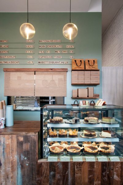 Café counter and menu wall inside Better Burnt, with rustic timber details and glass cake display.