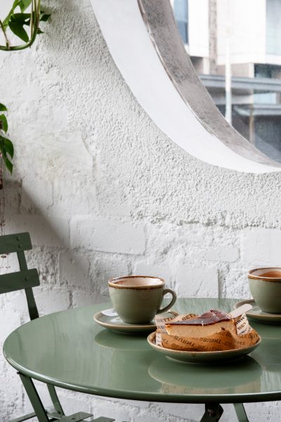 Small café table with green chairs, coffee cups, and burnt Basque cheesecake inside Better Burnt London.