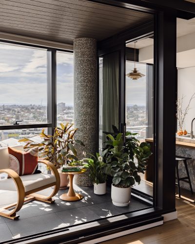 London apartment winter garden with tiled column, timber armchair, and layered plants.