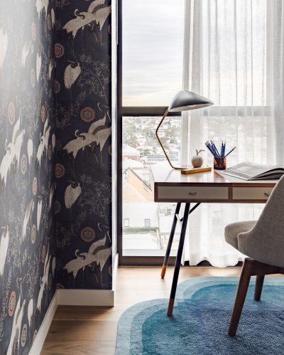 London apartment study corner with patterned wallpaper, desk, and blue rug.