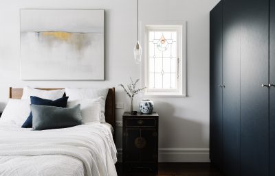 London bedroom interior with navy bespoke wardrobes, abstract artwork, and layered bedding.