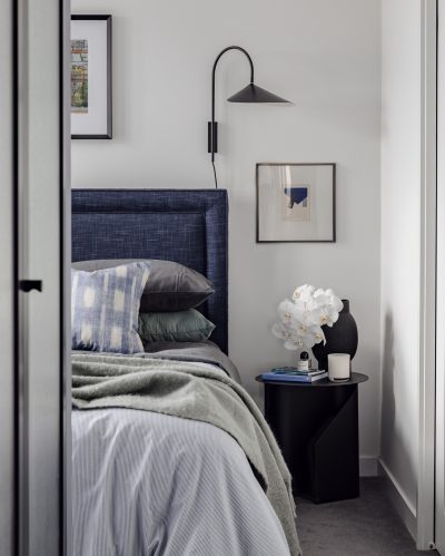 London apartment bedroom with upholstered blue headboard, layered bedding, and wall lighting.