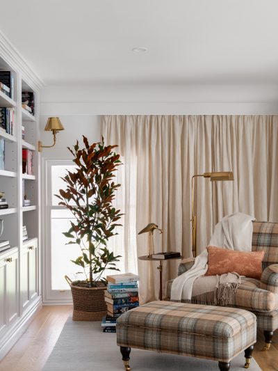 Cozy reading nook with plaid armchair, brass lighting, and built-in shelves in a London home library.