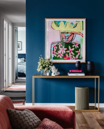 London apartment hallway with bold blue feature wall, contemporary artwork, and gold console table.