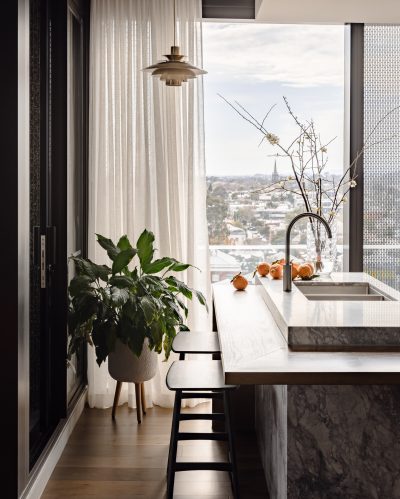 London apartment kitchen with marble island, soft sheer curtains, and indoor plants.