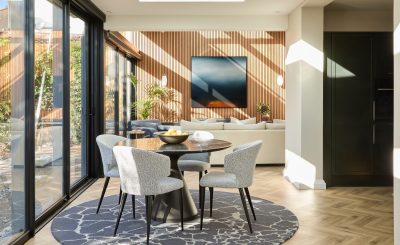 Modern London open-plan dining and living room with timber wall panels, marble dining table, and natural light.