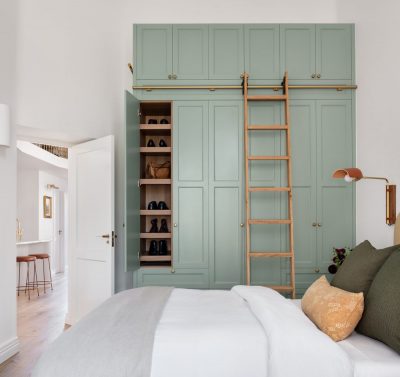 London bedroom with custom green joinery, rolling ladder, and layered bedding designed by The Stylesmiths.