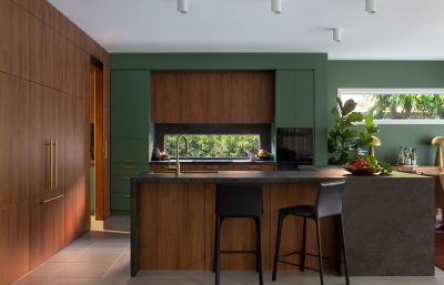 Modern London kitchen interior design with green cabinetry, wood finishes, and stone island by The Stylesmiths.