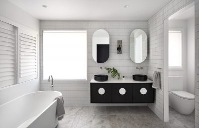 Finsbury bathroom with dual black basins, circular mirrors, and white tiled walls designed by The Stylesmiths London.