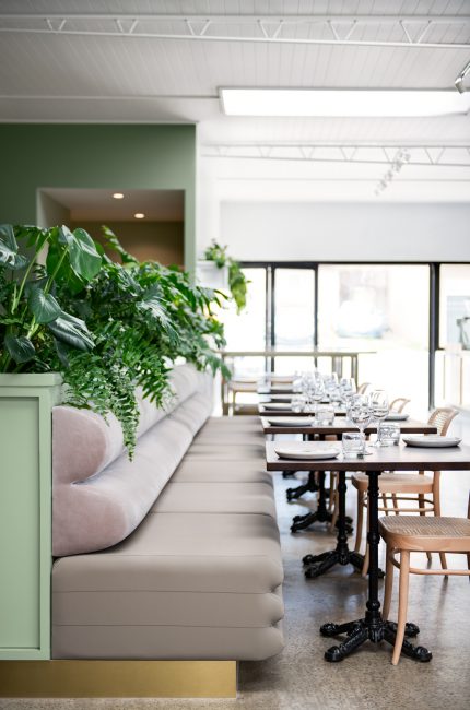 Fitzrovia restaurant interior with soft neutral banquette seating, green accents, and natural light designed by The Stylesmiths London.