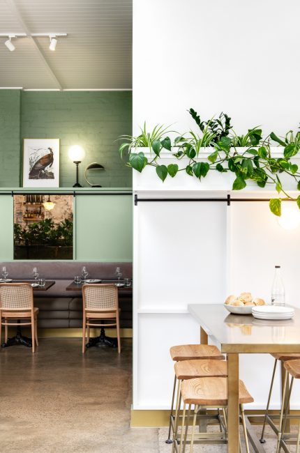 Contemporary Limehouse restaurant interior with green feature wall, timber furniture, and hanging plants by The Stylesmiths London.