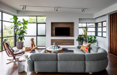 Spacious Limehouse living room with curved grey sofa, timber accents, and lush greenery designed by The Stylesmiths London.