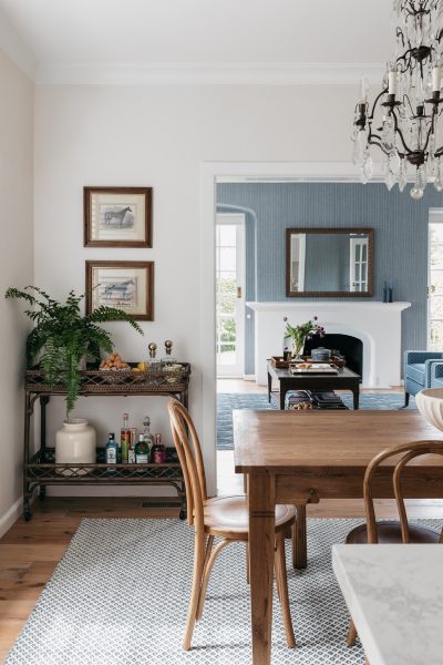 Dining room with chandelier, wooden furniture, and view to blue-toned living room in London home.