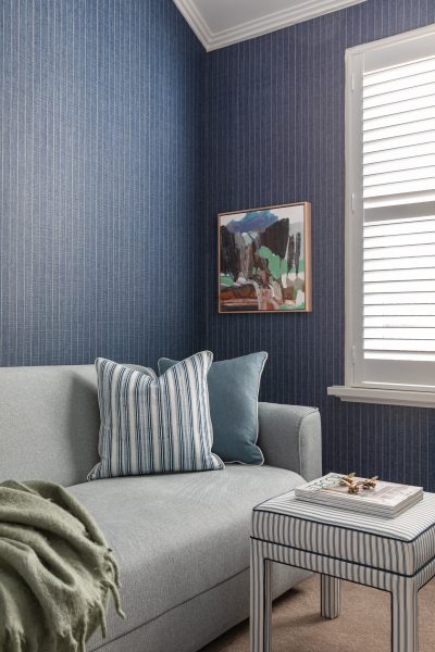 Blue sitting room with striped cushions, abstract artwork, and soft natural light designed by The Stylesmiths London.
