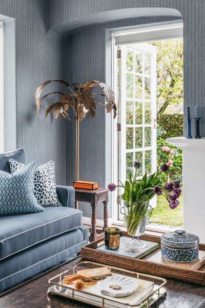 Living room with blue walls, gold palm lamp, and garden views designed by The Stylesmiths London.