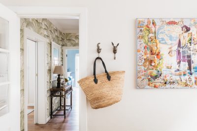 Hallway with tropical wallpaper, rattan furniture, and colourful artwork in a London home designed by The Stylesmiths.