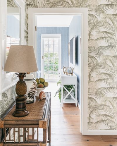 Hallway with palm leaf wallpaper, rattan console, and ceramic decor designed by The Stylesmiths London.