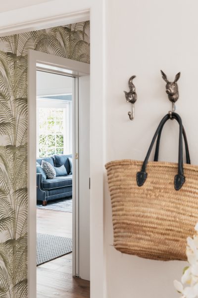 Hallway with palm wallpaper and view into blue living room in a London heritage home.