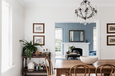 Dining area with chandelier and view into blue-toned living room designed by The Stylesmiths London.