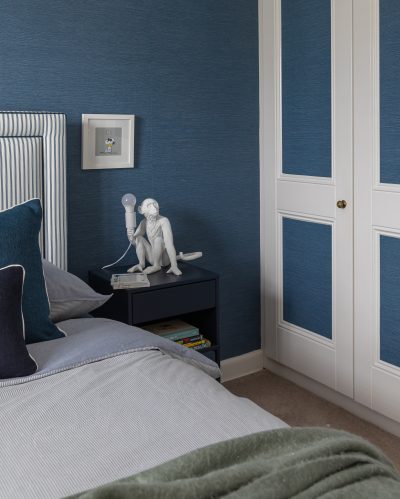 London bedroom with blue striped headboard, velvet cushions, and green throw designed by The Stylesmiths.
