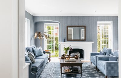 London living room with blue patterned wallpaper, white fireplace, and bespoke upholstered furniture.