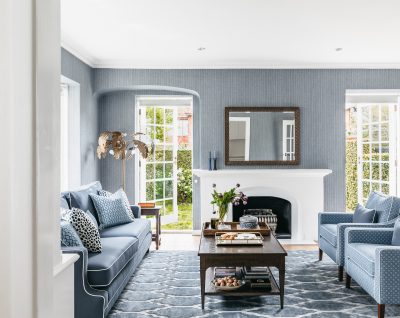 London living room with blue patterned wallpaper, white fireplace, and bespoke upholstered furniture.