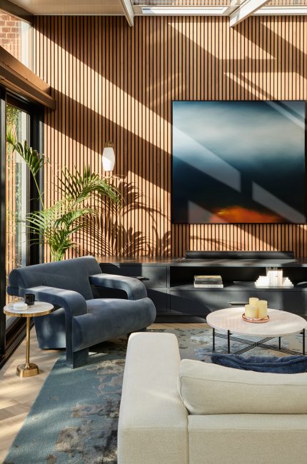 London living room with timber slat wall, large windows, and sunlight filtering across blue armchairs designed by The Stylesmiths London.