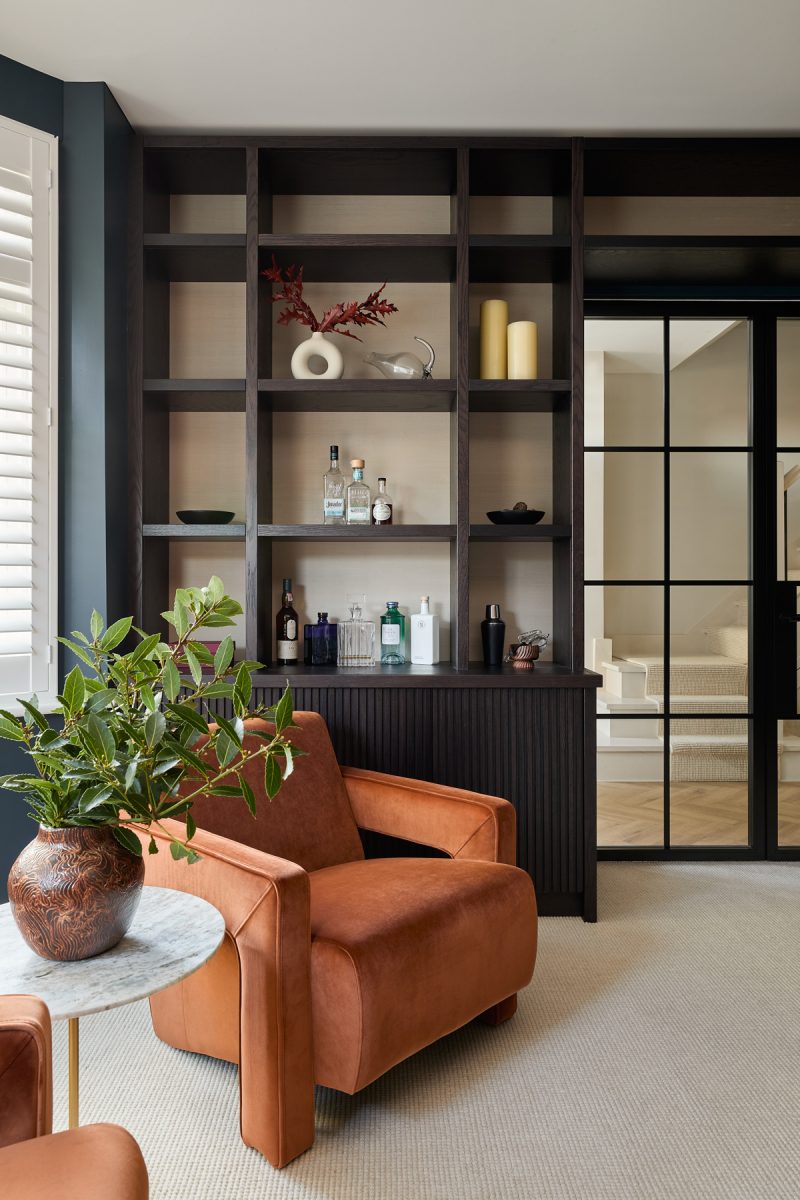 Contemporary London living room with terracotta armchairs and dark timber shelving by The Stylesmiths London.