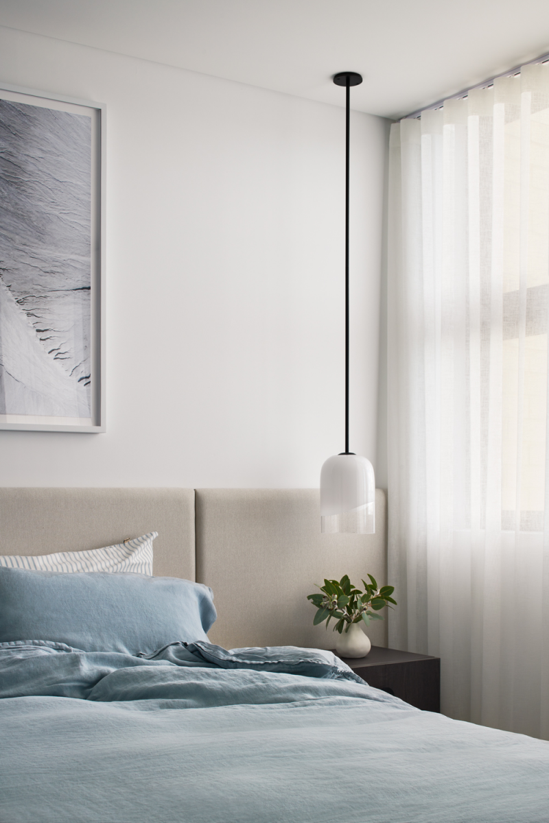 Modern London bedroom with soft blue bedding, minimalist pendant light and sheer curtains, styled in a calm neutral palette by The Stylesmiths.