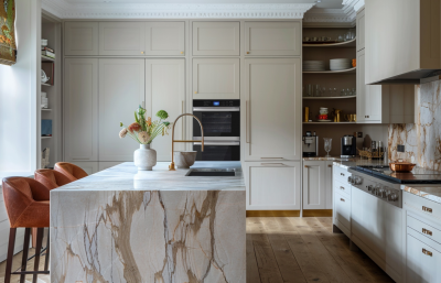 Modern London kitchen with marble waterfall island, light cabinetry and warm leather bar stools, styled with refined materials by The Stylesmiths.