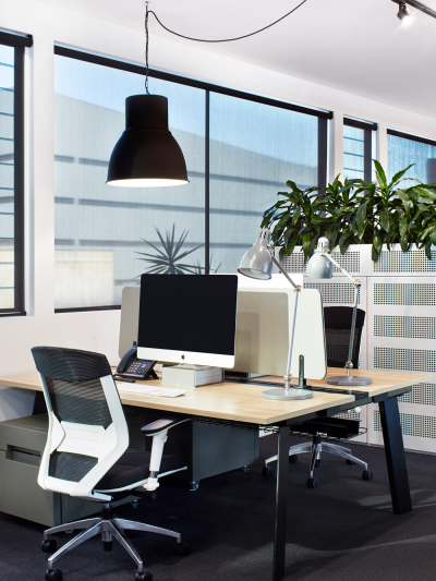 Modern London office interior with minimalist desk setup, black pendant light, task lamps and indoor plants in a bright workspace by The Stylesmiths.