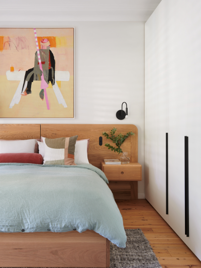 Scandinavian bedroom with oak bedhead, crisp white walls, soft pastel artwork and calm layered linens.