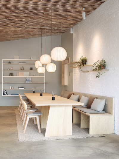 Scandinavian co-work space with light timber communal table, paper pendant lights, built-in bench seating and calm neutral tones.