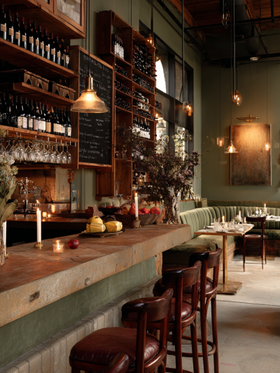 Sustainable London hospitality interior with warm industrial styling, reclaimed timber shelving, ambient pendant lighting and stone bar counter by The Stylesmiths.